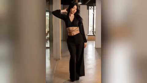 Elegant woman in a black long-sleeve crop top and wide-leg trousers posing in a modern minimalist interior.