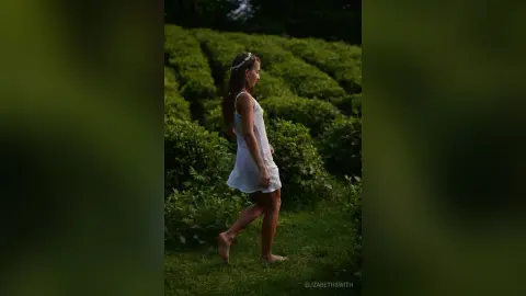 Young woman in a white summer dress walking through a lush green garden at twilight.