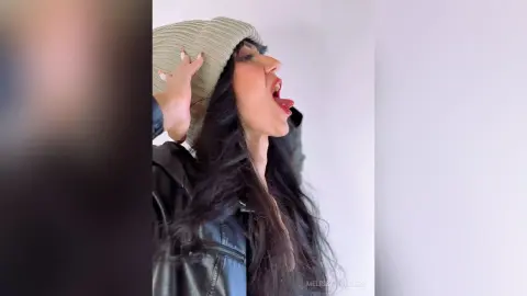 Cheerful woman in a black leather jacket and beige knit beanie laughing against a white background.