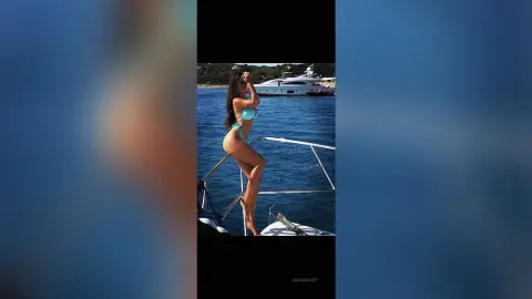 ArianaKroft poses in a light blue bikini on a boat, standing against a backdrop of blue ocean water.