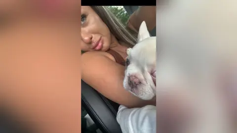 KaylaDepp poses closely with a white dog, showing her face, long brown hair, and bare shoulder in a car setting.