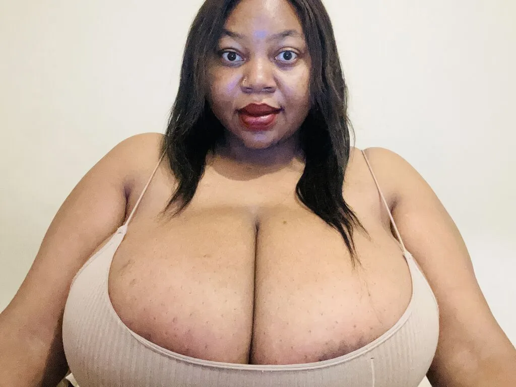 PamelaForbes — PamelaForbes looks directly at the camera wearing a tan ribbed tank top that accentuates her large breasts.