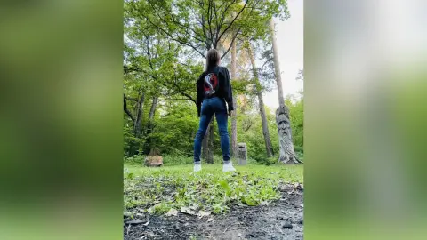 Woman in black long-sleeve shirt and blue jeans standing in a lush green forest setting.