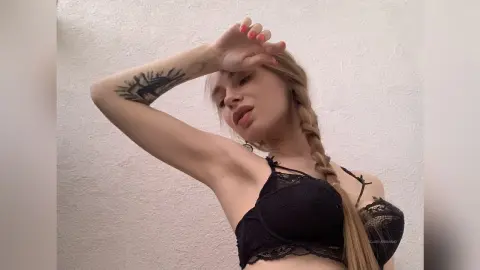 Young woman with blonde braid in black lace lingerie posing against a white wall with a relaxed mood.
