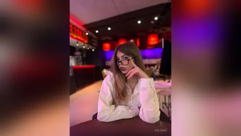 Stylish woman in a white shirt and glasses sitting at a restaurant table with moody red lighting.