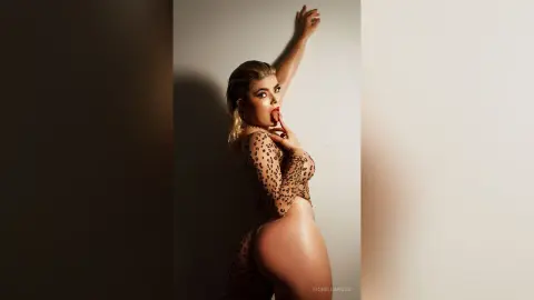 FiorellaRossi poses with one arm raised, wearing a sheer black polka-dot bodysuit that reveals her bare buttocks.