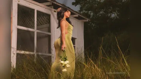 Elegant woman in a long yellow gown holding white roses in a dreamy outdoor meadow setting.