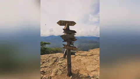 RossiNoleen's photo features a wooden signpost pointing toward El Salto, standing on a rocky cliffside overlooking a vast mountain valley under a cloudy sky.