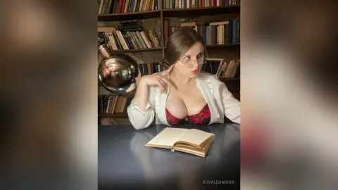 KuvaldaNadin — KuvaldaNadin sits at a desk with an open book, wearing glasses and a red lace bra under an open white shirt.