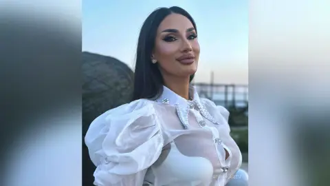 AnnaKarev poses outdoors in a white sheer blouse with puffy sleeves and crystal details.