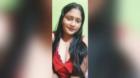 QueenPori poses with long black hair wearing a red lace camisole against a light green wall.