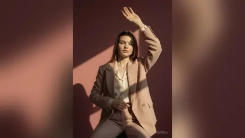 Elegant woman in a beige blazer and white silk blouse posing in warm sunlight for a sophisticated fashion look.
