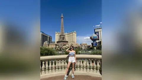 Young woman in a white crop top and shorts posing by a fountain with the Paris Las Vegas Eiffel Tower background.