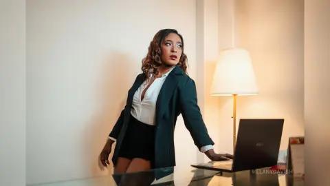 Confident professional woman in a black blazer and white blouse standing in a modern office setting.