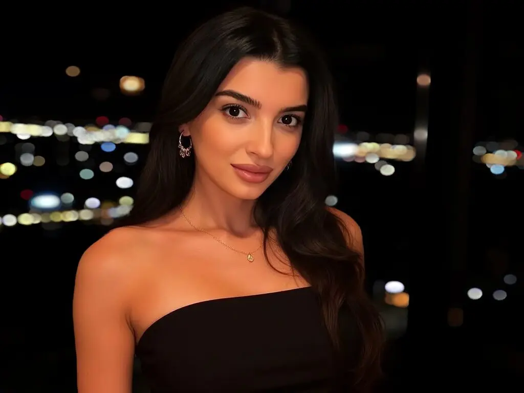 Beautiful woman in a black strapless dress posing against a blurred city night skyline.