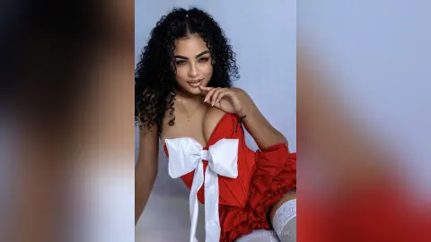 Beautiful woman with curly hair wearing a red corset with a white bow in a soft studio setting.