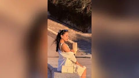 Young woman in a white summer dress sitting on stone stairs during a warm golden hour sunset.