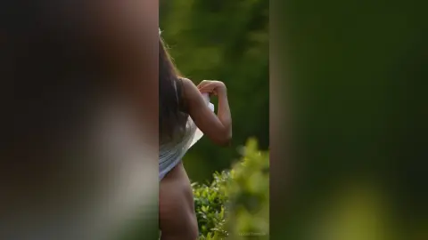 Young woman in a white summer dress standing in a lush green garden during golden hour.
