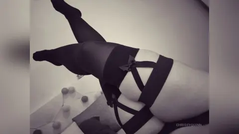 Close-up of a woman in black stockings and a lace garter belt lying on a white surface in a moody aesthetic.