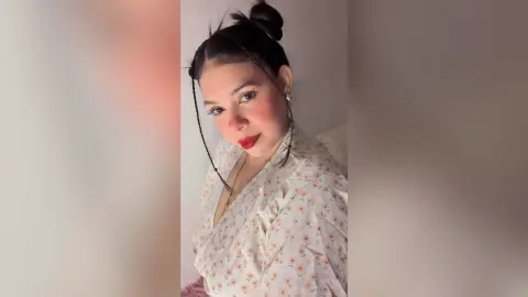 Smiling woman in a floral print blouse posing indoors with a soft, natural aesthetic.