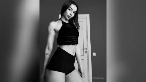 Young woman in black halter crop top and shorts posing in a minimalist indoor setting with a moody aesthetic.