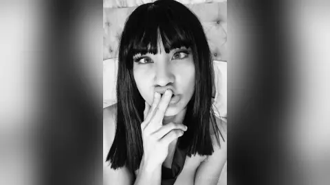 Close-up portrait of a young woman with long black hair and bangs looking into the camera in a moody black and white style.