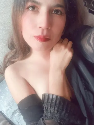 Zharid_Parker poses closely in a black top with her hand resting against her neck and long brown hair falling over her shoulders.