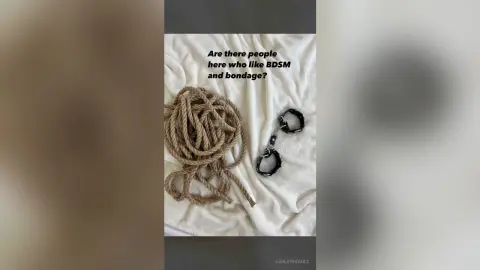 Coiled hemp rope and metal handcuffs resting on a white textured fabric surface for a minimalist BDSM aesthetic.