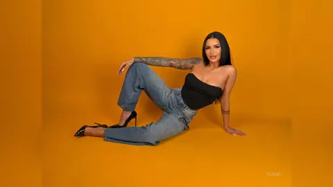 Stylish woman in black tube top and blue jeans sitting on a bright yellow background.
