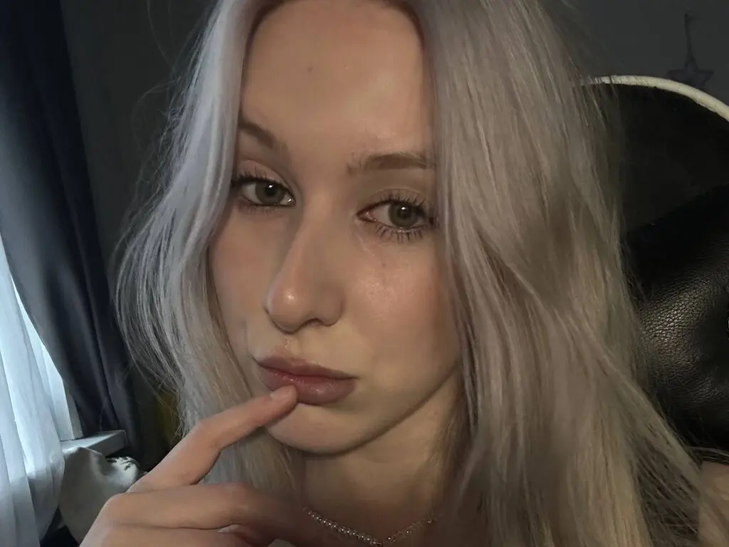 ElviStars poses close-up with her long, light blonde hair, touching her lip with one finger while looking into the camera.