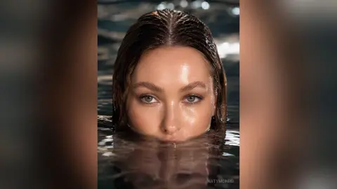 KatyMonro looks directly at the camera with wet hair while partially submerged in dark water.