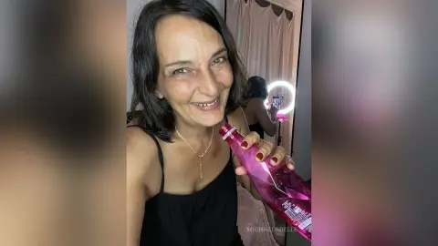 MichaelaBelle smiles while holding a pink bottle of water against her black camisole top.