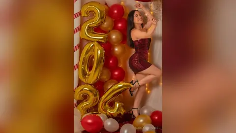 Cheerful woman in a sparkling red sequin dress posing with gold and red balloons for a New Year celebration.