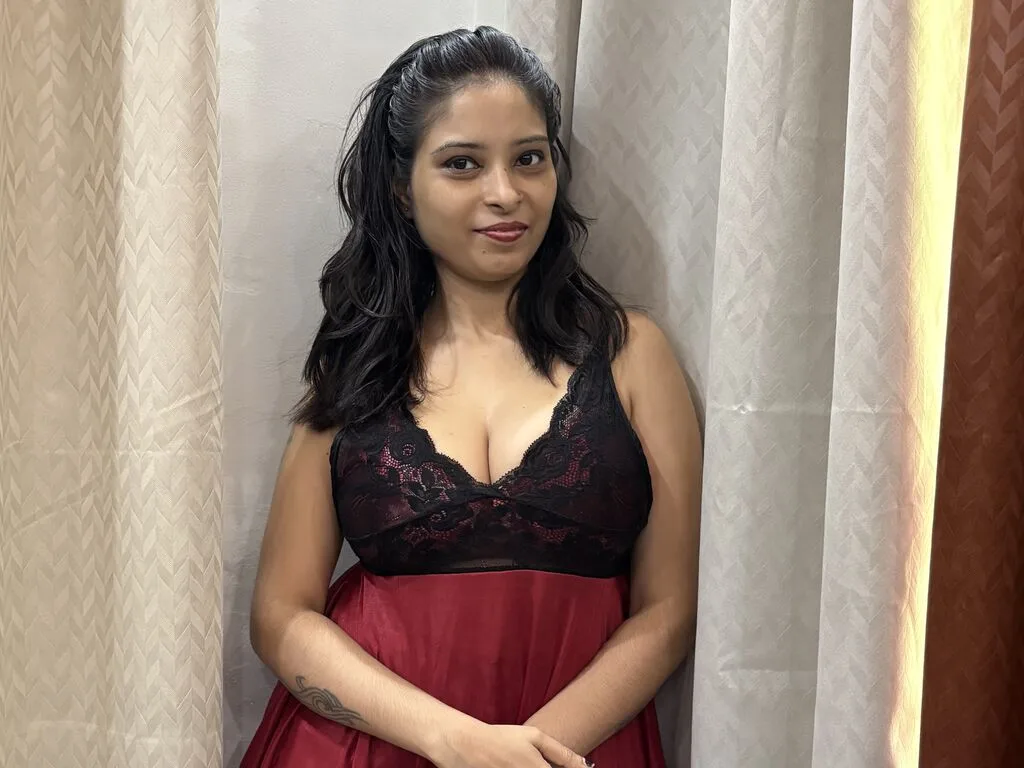 KiaraMuse — KiaraMuse sits on a brown sofa wearing a black lace camisole with white trim, looking at the camera.