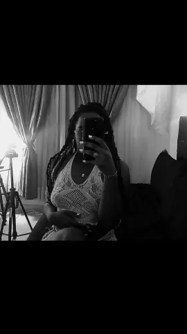 Black woman with long braids wearing a white lace tank top taking a moody selfie in a dimly lit room.