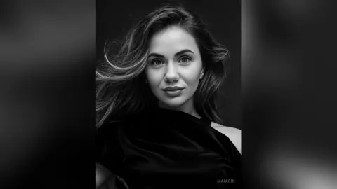 Portrait of a smiling woman with flowing hair wearing a black satin dress in a moody black and white studio setting.