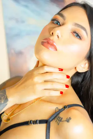 Close-up portrait of a woman with glowing makeup and dark hair wearing a black lace bra in a bright setting.