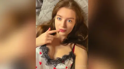 Young woman with long brown hair wearing a white lace camisole relaxing in a cozy indoor setting.