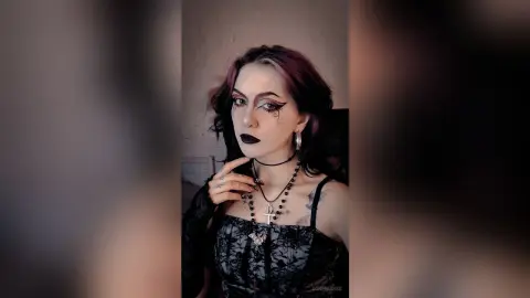 Gothic woman with dark makeup and silver cross necklace posing in moody aesthetic attire.