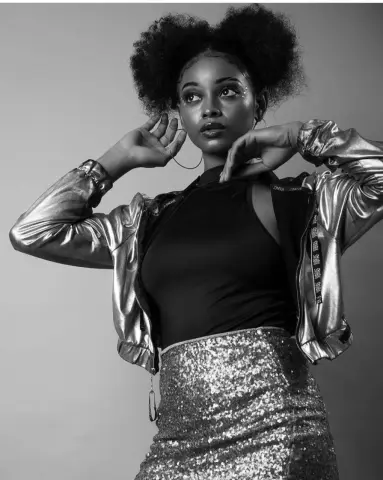 Stylish woman in a metallic jacket and sequin skirt posing confidently in a studio setting.