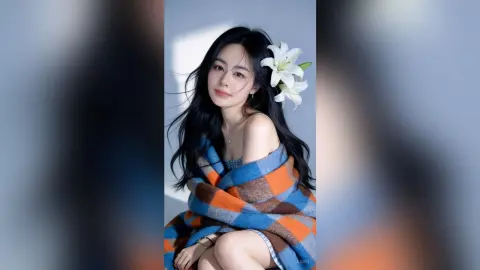 Beautiful woman with long dark hair wrapped in a blue and orange plaid blanket against a soft light background.
