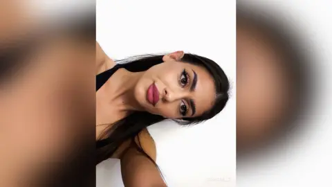 Glamorous woman with bold makeup and dark hair wearing a black top against a clean white background.