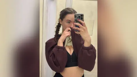 Young woman with braided hair wearing a maroon cropped jacket and black sports bra in a mirror selfie.