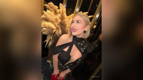Glamorous blonde woman in a black cutout evening gown posing elegantly near golden floral decor.