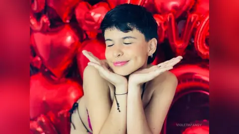 Smiling young woman with short hair posing playfully against a romantic red heart background.