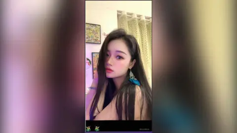 Young woman with long dark hair wearing blue tassel earrings in a cozy indoor setting.