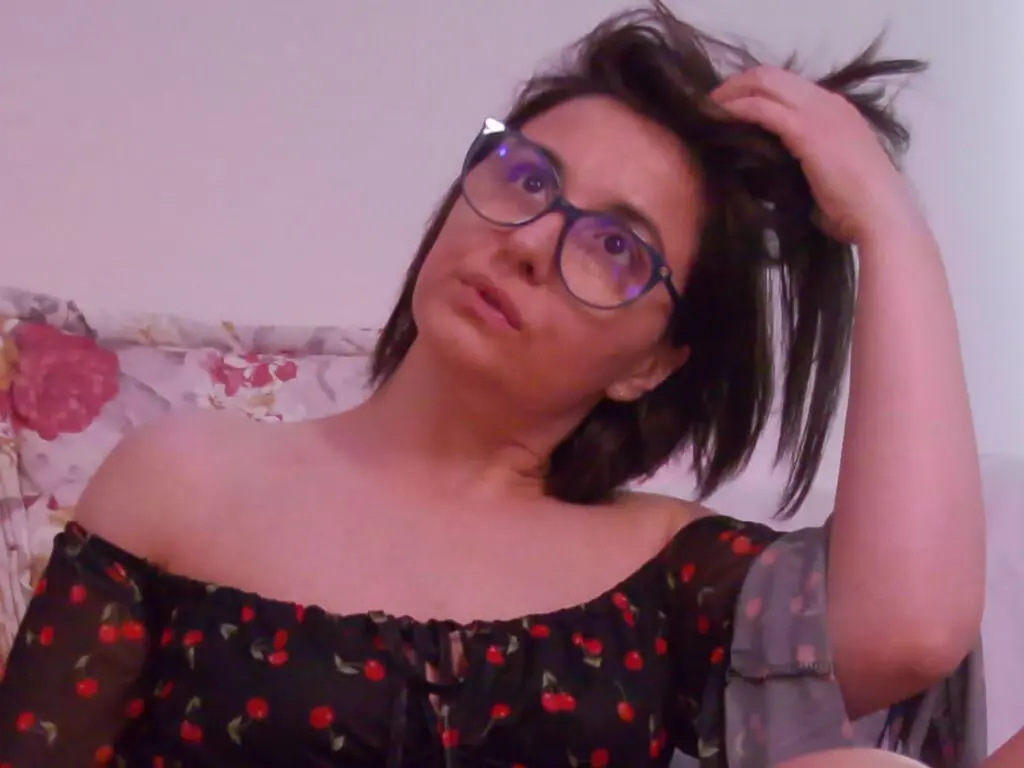Woman in black floral off-the-shoulder top wearing glasses and relaxing at home with a thoughtful mood.