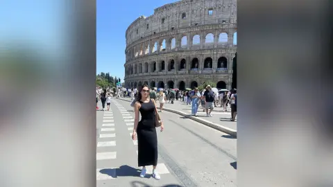 Stylish woman in a black midi dress and white sneakers walking near the Roman Colosseum on a sunny day.