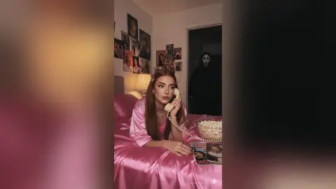 Young woman in pink satin pajamas talking on a vintage phone in a moody, cinematic bedroom setting.
