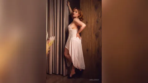 AmeliaReds — AmeliaReds poses in a white lace chemise while leaning against a wooden wall next to a curtain.